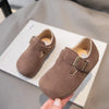 A pair of brown retro non-slip kids' moccasin shoes with a hook-and-loop closure resting on a white box.