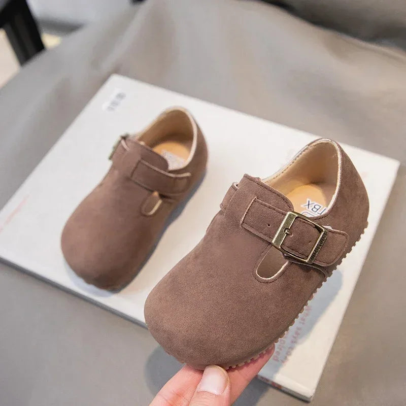 A pair of brown retro non-slip kids' moccasin shoes with a hook-and-loop closure resting on a white box.