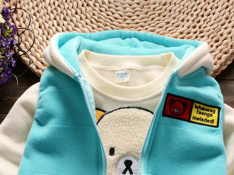 A light blue fleece jacket and matching top with a cartoon bear design, displayed on a woven mat.