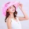 A woman wearing a pink wide brim organza sun hat with ruffled mesh and a white top.