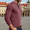 A man wearing a maroon long-sleeve casual shirt with a chest pocket, standing in a European square.