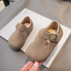 A pair of tan suede kids' moccasin shoes with a hook-and-loop closure resting on a white surface.