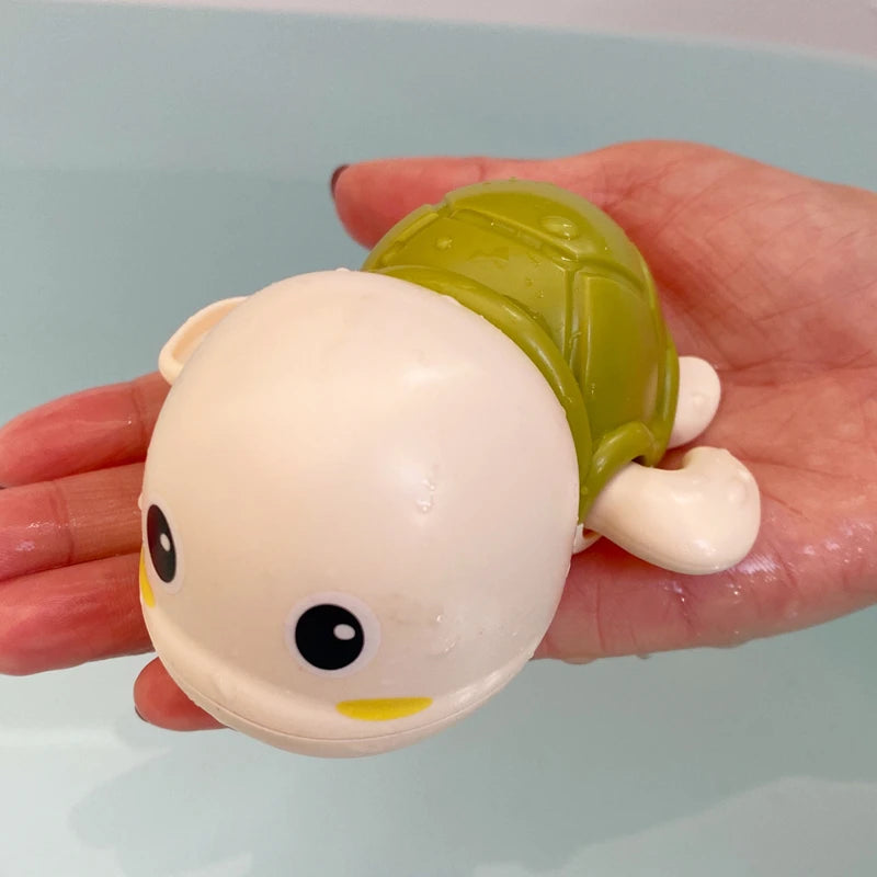 A hand holds a cute bath toy shaped like a duck with a green shell and a light pink body.