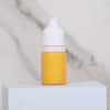 A small glass bottle of yellow liquid paint with a white dropper cap sitting on a white surface.