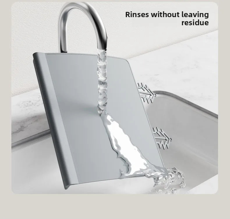 A silver silicone feeding placemat with a textured teething edge is shown being rinsed without leaving residue.