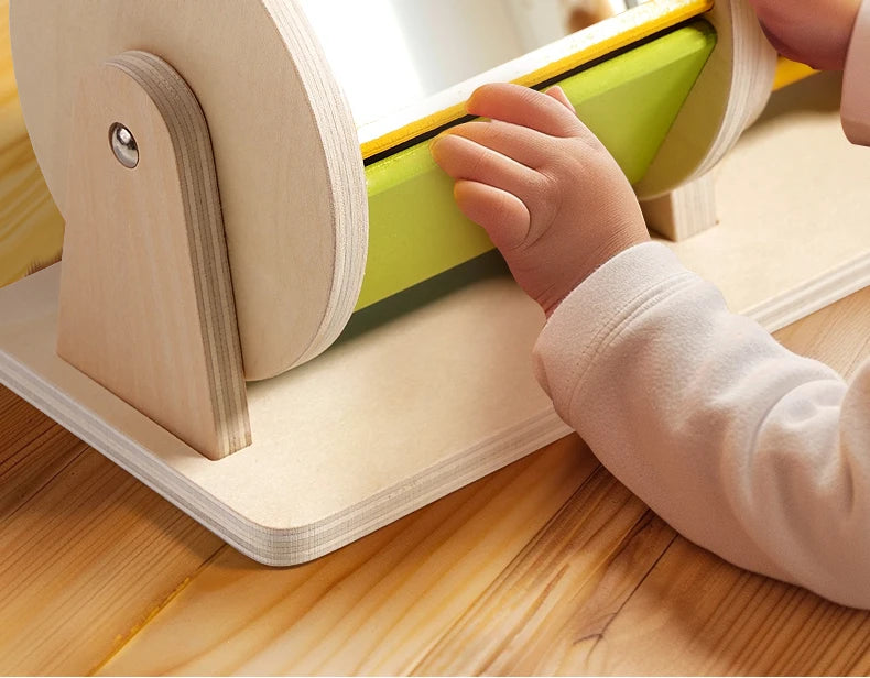 A toddler is interacting with a wooden spinning drum toy designed for Montessori play.
