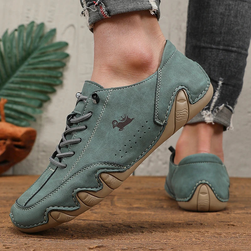 A close-up of a pair of sage green men's classic lace-up loafers resting on a wooden surface.