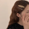A close-up of a woman's hair showing two matte resin side clips used to style her long brown hair.