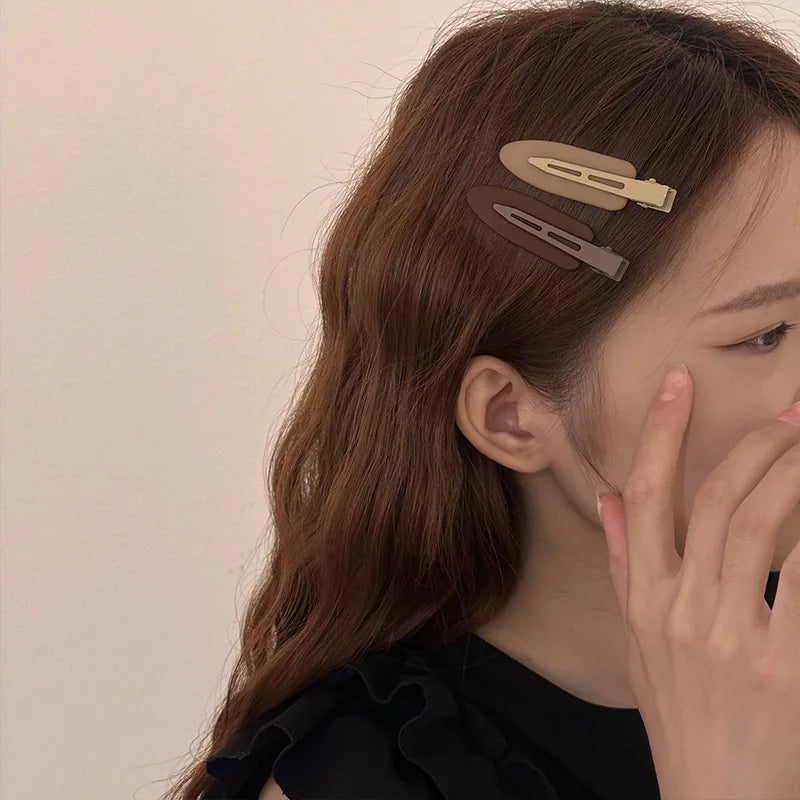 A close-up of a woman's hair showing two matte resin side clips used to style her long brown hair.