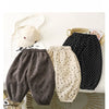 A pair of dark gray fleece-lined pants with small black polka dots, displayed next to a beige cap and a woven basket.
