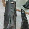 A black knee-high chunky heel boot with a metal buckle is shown on a person's foot.