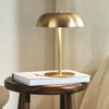A modern brass portable touch table lamp with a dome shade rests on a stack of white books.