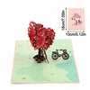 A pink card featuring a red tree silhouette and a bicycle silhouette on a light green background.