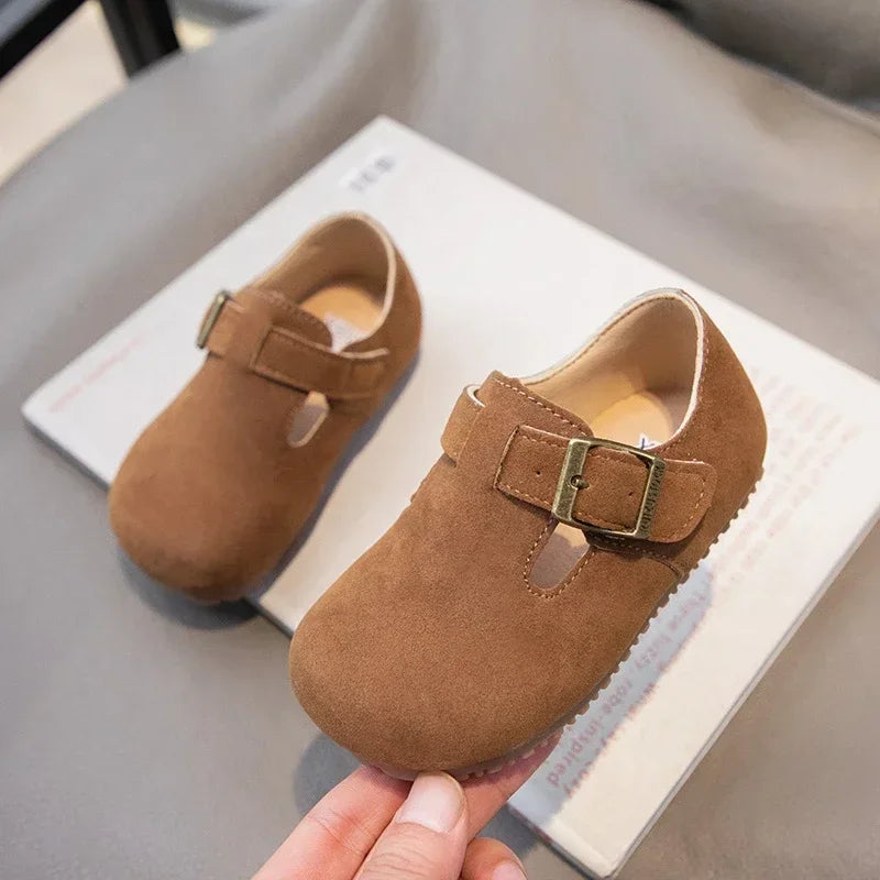 A pair of brown retro non-slip kids' moccasin shoes with a leather hook-and-loop closure resting on a white card.