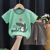 A green dinosaur print kids' short-sleeve t-shirt and shorts set displayed on a wooden hanger.