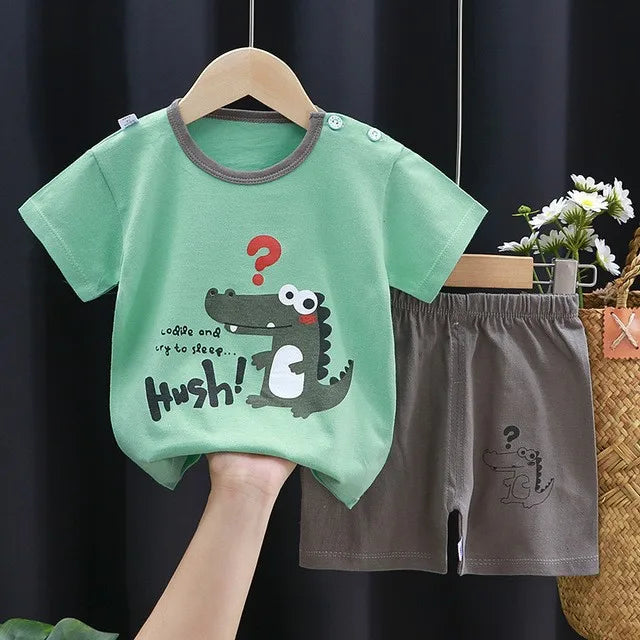 A green dinosaur print kids' short-sleeve t-shirt and shorts set displayed on a wooden hanger.