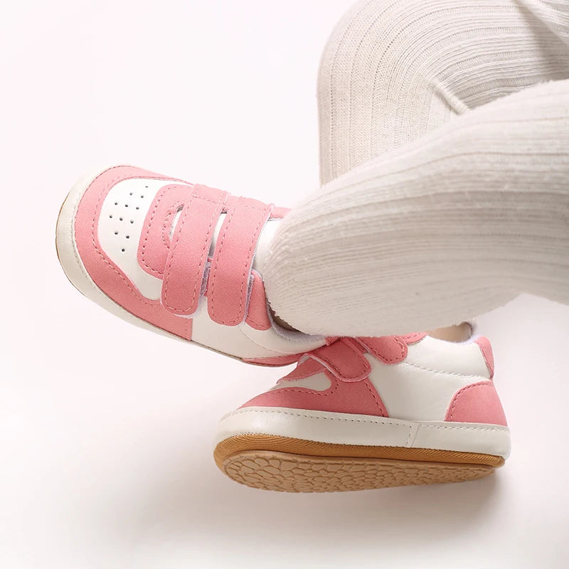 A close-up of pink and white soft sole baby pre-walker sneakers worn on a person's foot.