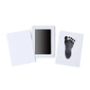 A white frame holds a black handprint and footprint keepsake on a white card.