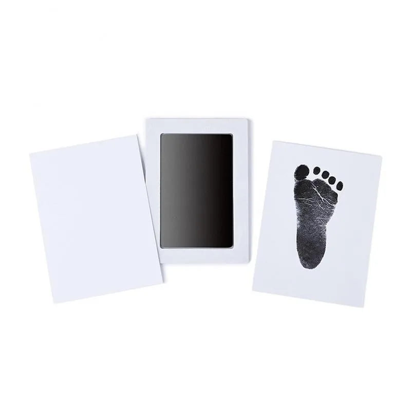 A white frame holds a black handprint and footprint keepsake on a white card.