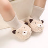 A pair of cute cartoon baby booties made of light beige felt with brown accents, shown on a person's foot.