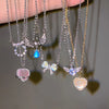 A collection of silver and gold crystal bow angel wings heart pendant necklaces displayed on a hand.