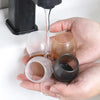 A hand is pouring liquid onto silicone furniture leg pads with felt bottoms for scratch protection.