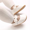 A close-up of soft white baby first walker shoes with floral accents on a person's foot and ankle.