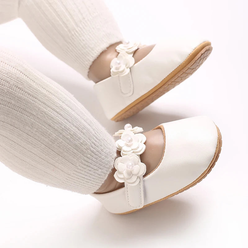 A close-up of soft white baby first walker shoes with floral accents on a person's foot and ankle.