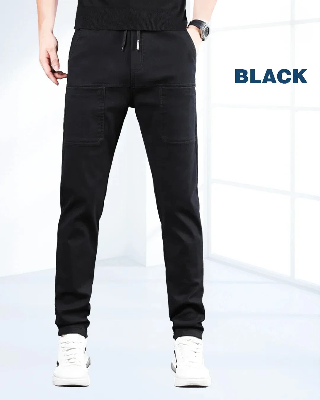 En mand iført sorte stretch-cargobukser med hvide sneakers, set forfra.
