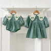 A teal kids princess dress with floral embroidery and lace trim hanging on a white shelf.