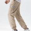 A man wearing beige cargo joggers and a white shirt, with a black watch on his wrist.