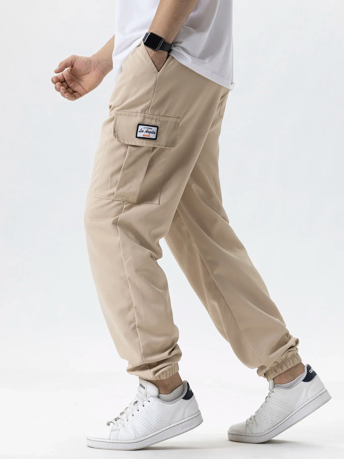 A man wearing beige cargo joggers and a white shirt, with a black watch on his wrist.