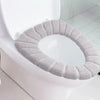 A light gray, textured acrylic toilet seat cover is placed on a white toilet bowl.