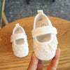 A hand holds a pair of white soft non-slip baby first walker shoes with lace detailing.