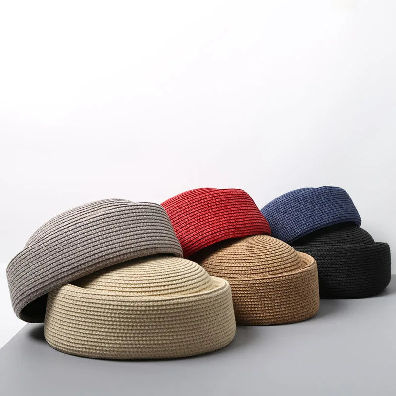 A collection of straw pillbox sun hats in various shades including gray, red, blue, and beige, displayed on a gray surface.
