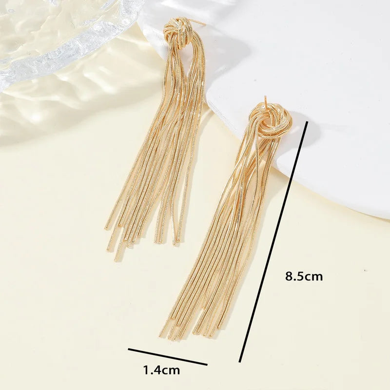 A pair of gold geometric tassel drop earrings displayed against a light background.