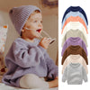 A baby wearing a purple knitted long-sleeve pullover sweater and a matching knitted hat.