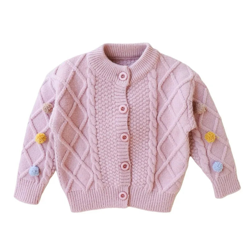 A pink knitted cardigan sweater for girls featuring a diamond pattern and pom-pom trim.
