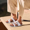 A pair of beige women's cork footbed slide sandals with white straps resting on a light surface.