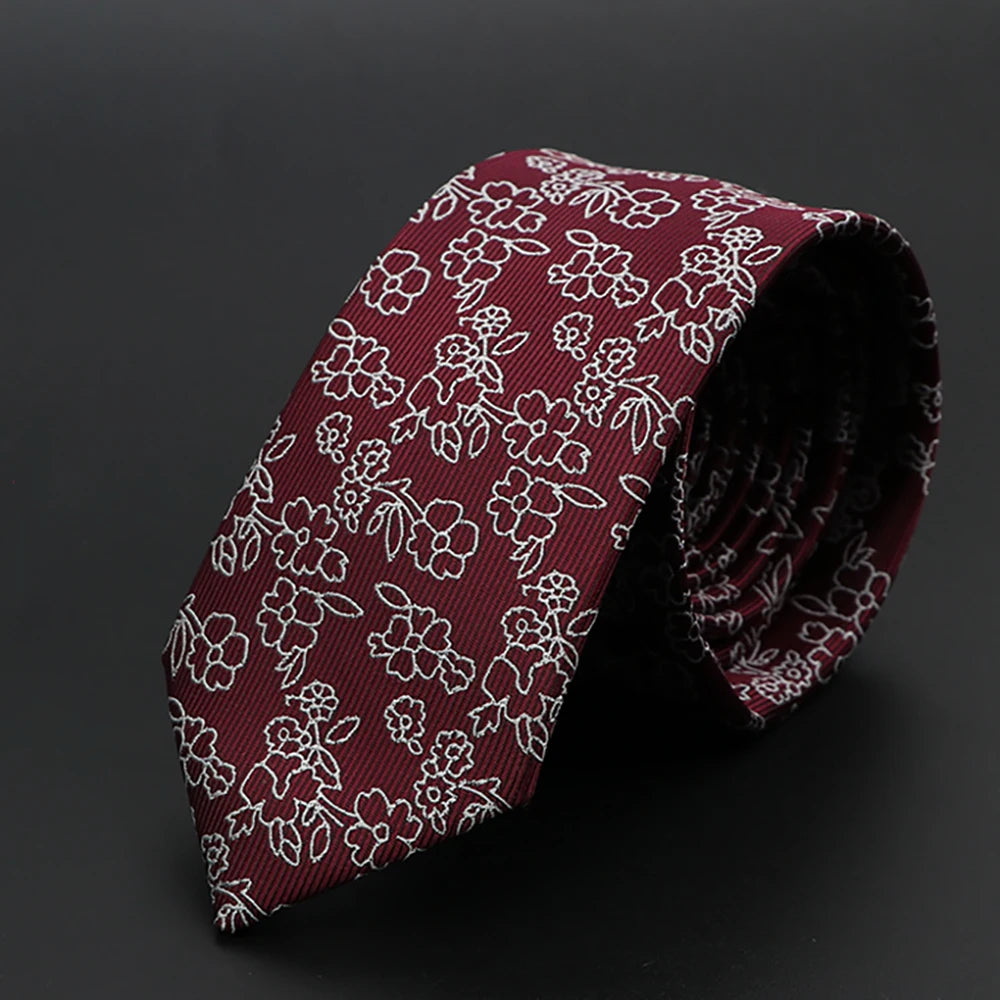 Corbata granate con diseño floral blanco, enrollada sobre fondo oscuro.