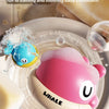 A pink and white musical light-up whale baby bath toy with a water spray is shown in use in a bathtub.