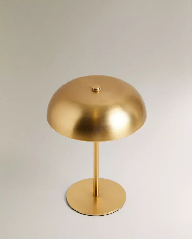 A brass-colored portable touch table lamp with a dome shade mounted on a circular base.