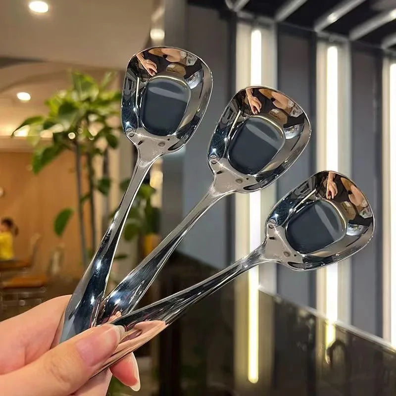 A hand holds three stainless steel serving spoons with long handles against a blurred background.