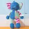 Muñeco de peluche elefante azul con orejas y cuerpo de rayas rosas y verdes, sentado sobre una superficie clara.