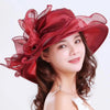 A woman wearing a wide brim organza sun hat with ruffled mesh in deep red and brown hair.