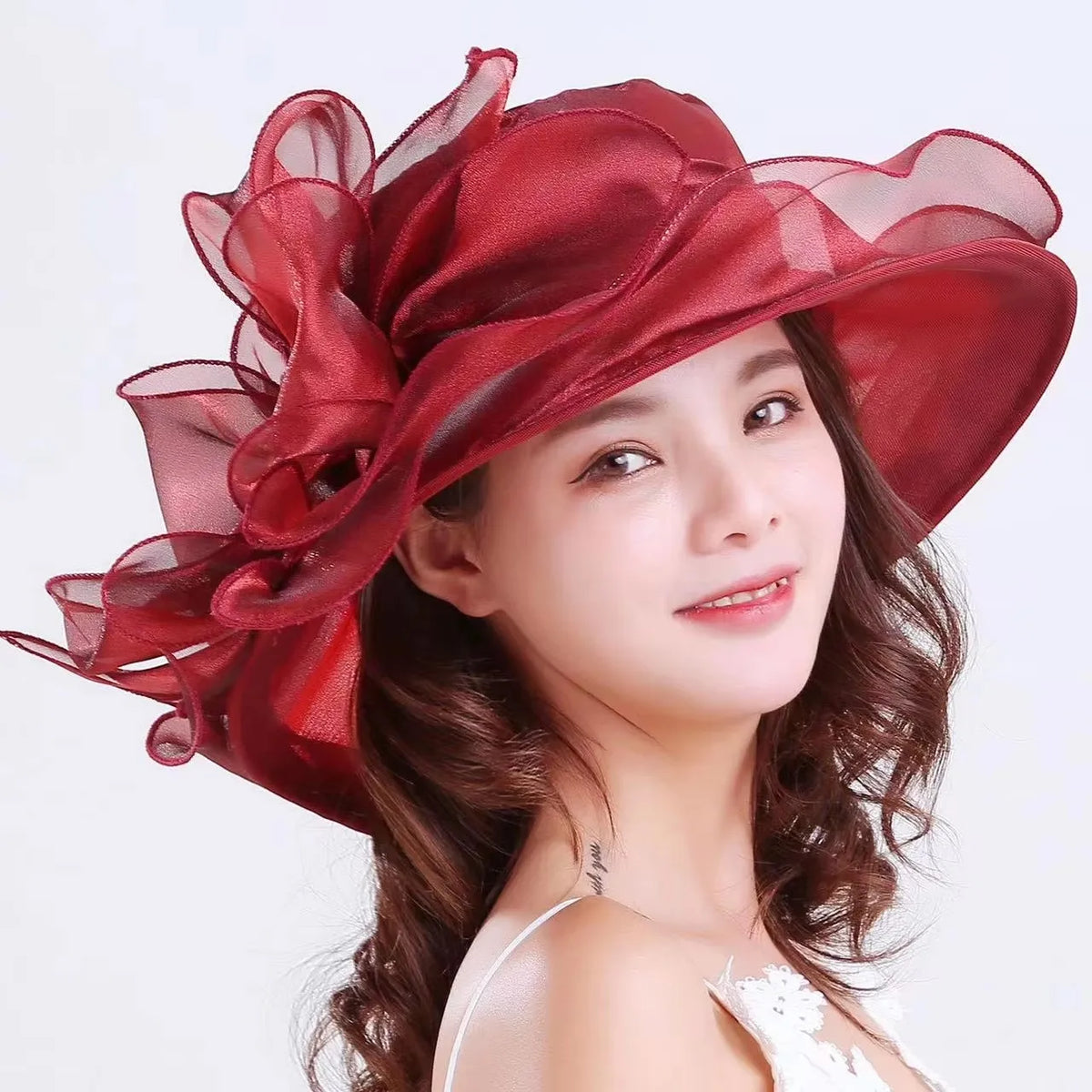 A woman wearing a wide brim organza sun hat with ruffled mesh in deep red and brown hair.