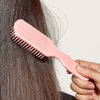 Una mano sostiene un peine desenredante rosa de nueve púas sobre cabello oscuro.
