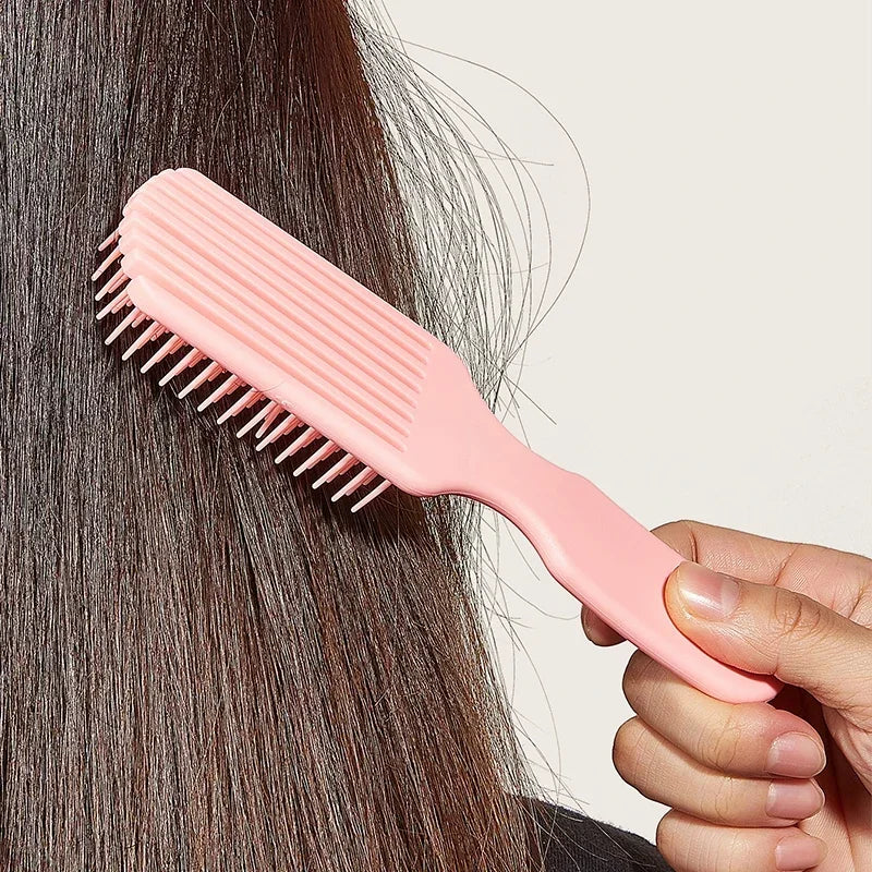 Una mano sostiene un peine desenredante rosa de nueve púas sobre cabello oscuro.