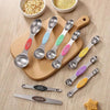 A set of nine stainless steel double-headed measuring spoons with magnetic storage displayed on a wooden board.