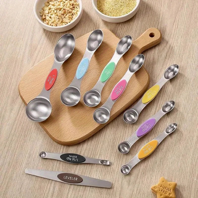 A set of nine stainless steel double-headed measuring spoons with magnetic storage displayed on a wooden board.